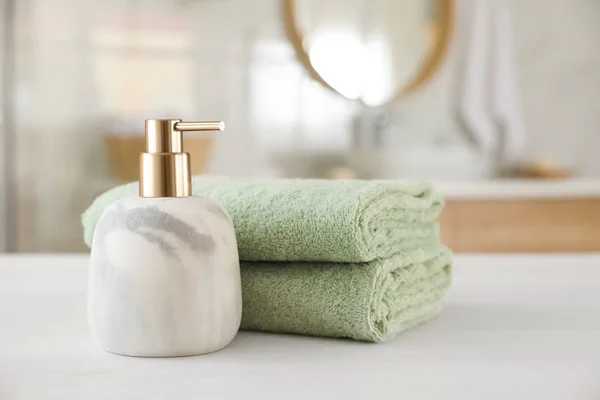 Czyste ręczniki i dozownik mydła na białym drewnianym stole w szlafroku — Zdjęcie stockowe