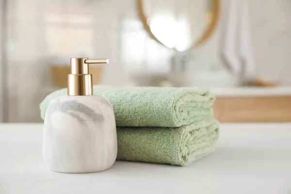 Clean towels and soap dispenser on white wooden table in bathroo — Stock Photo, Image