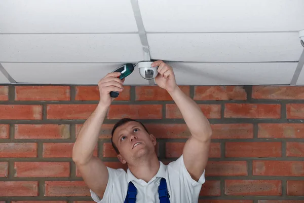 Техник устанавливает камеру видеонаблюдения на потолке в помещении — стоковое фото