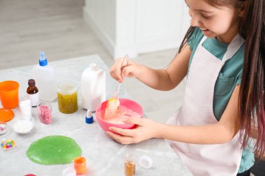 Küçük kız, içerideki masada silikon spatulayla karıştırıyor, yakın plan. Çamur oyuncağı