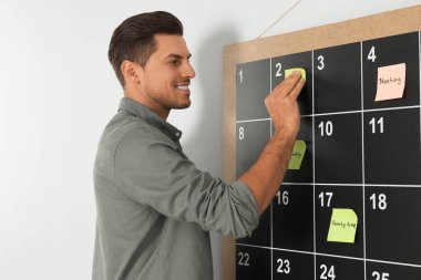 Yakışıklı adam takvime yapışkan not bırakıyor.