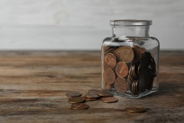 Ahşap masada bozuk paralarla dolu cam kavanoz, metin için boşluk