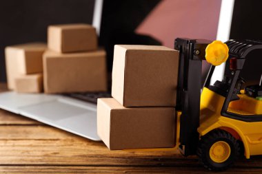 Oyuncak forklift, tahta masada dizüstü bilgisayarın yanında kutular. Lojistik ve toptan satış kavramı