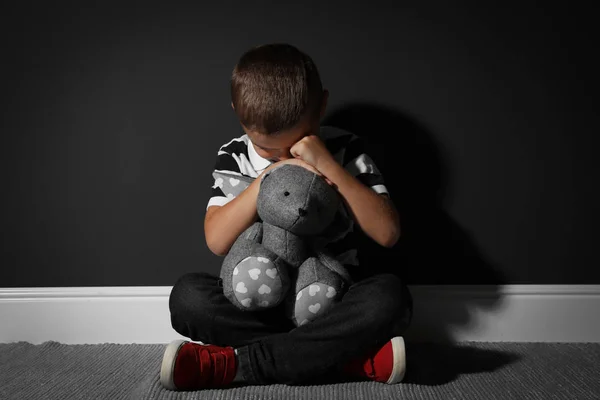 Испуганный маленький мальчик с игрушкой возле черной стены. Домашнее насилие — стоковое фото