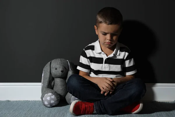 Menino triste com brinquedo perto da parede preta. Violência doméstica — Fotografia de Stock