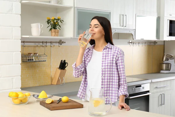 Красива молода жінка п'є лимонну воду на кухні — стокове фото