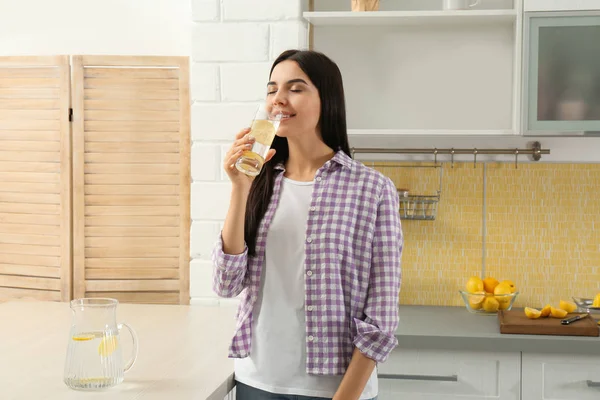 Vacker ung kvinna dricker citronvatten i köket — Stockfoto
