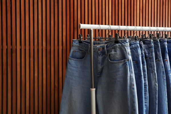 Rack with different jeans on wooden background, closeup. Space f — Stock Photo, Image
