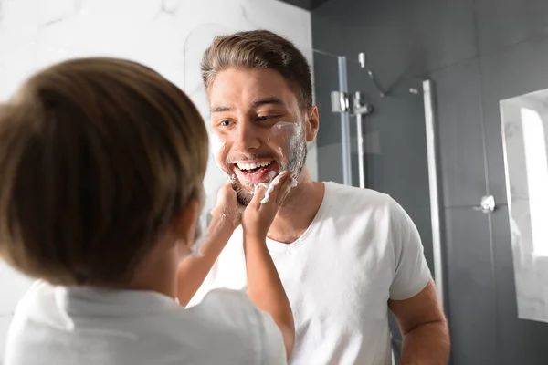 Dad and son with shaving foam on their faces having fun in bathr — ストック写真