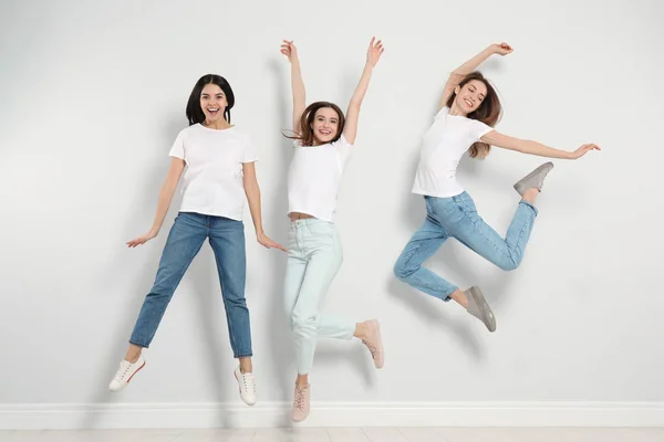 Grupo de mujeres jóvenes en jeans elegantes saltando cerca de la pared de luz —  Fotos de Stock