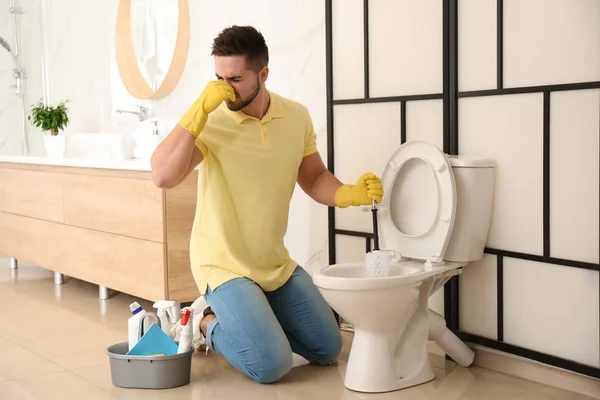Jovem sentindo nojo ao limpar vaso sanitário no banheiro — Fotografia de Stock