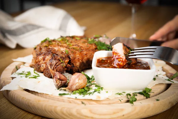 Woman eating delicious grilled pork chop at wooden table, closeup