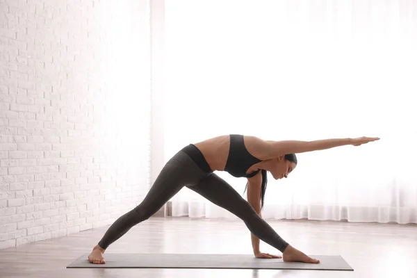 Junge Frau praktiziert Dreieck-Asana im Yoga-Studio. utthita tr — Stockfoto