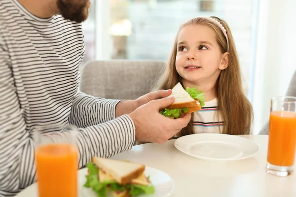 Otec a dcera mají snídani se sendviči u stolu v — Stock fotografie