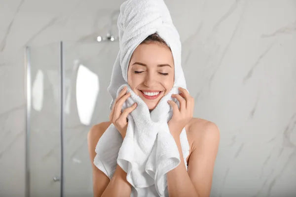 Young woman wiping face with towel in bathroom — Stok fotoğraf