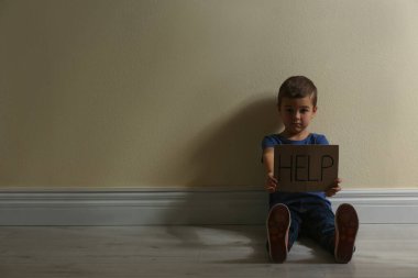 İşaretli küçük çocuk. Sarı duvarın yanında yerde oturmaya yardım et. Mesaj için yer aç. Çocuk tehlikede.