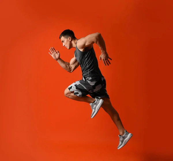 Atletisk ung man kör på röd bakgrund, sidovy — Stockfoto