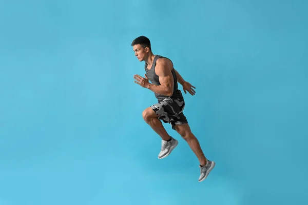 Atletický mladý muž běží na světle modrém pozadí, boční pohled — Stock fotografie