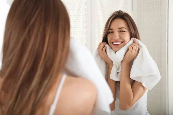 Mladá žena otírání tvář s ručníkem v blízkosti zrcadla v koupelně — Stock fotografie