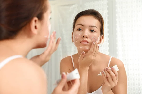 Chica adolescente con problemas de acné aplicando crema cerca del espejo en bathro — Foto de Stock