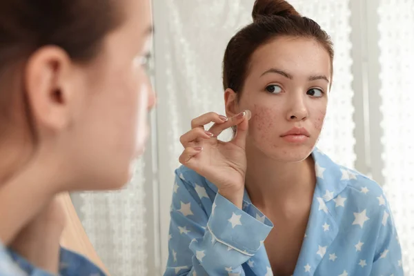 Teen girl applying acne healing patch near mirror in bathroom — Stock Photo, Image