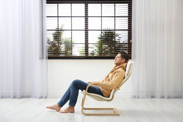 Attractive man relaxing in armchair near window at home