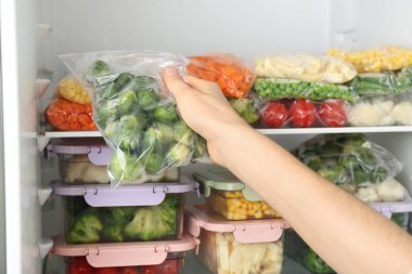 Buzdolabına Brüksel lahanası ve donmuş sebzelerle plastik poşet koyan bir kadın.