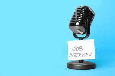 Retro microphone and reminder note with words JOB INTERVIEW on light blue background, space for text clipart