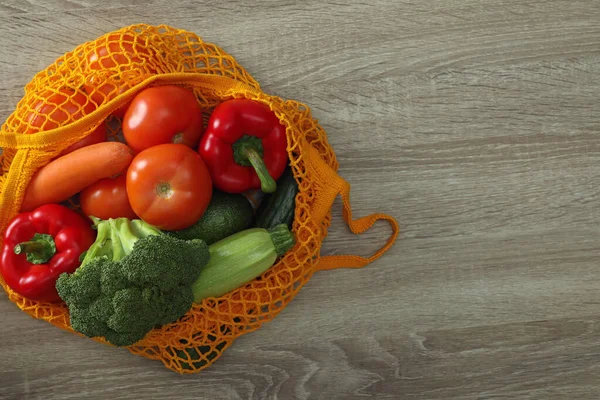 Bolsa de rede com legumes na mesa de madeira, vista superior. Espaço para tex — Fotografia de Stock