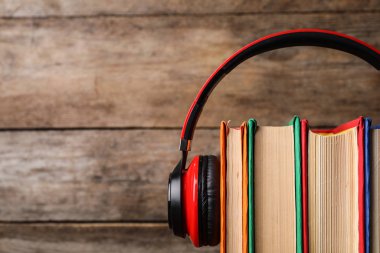 Kitaplar ve modern kulaklıklar ahşap arka planda, yakın plan. Metin için boşluk