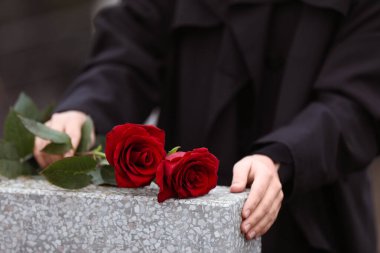 Açık gri mezar taşının yanında kırmızı gülleri olan kadın, yakın plan.