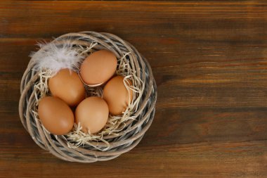 Tahta masada hasır yuvada çiğ tavuk yumurtası ve tüy, üst manzara. Metin için boşluk