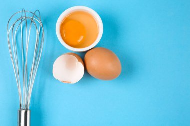 Çiğ yumurta ve açık mavi arka planda çırpılmış çırpılmış çırpılmış çırpılmış çırpma, yazı için yeri olan üst manzara. Pasta yapmak.