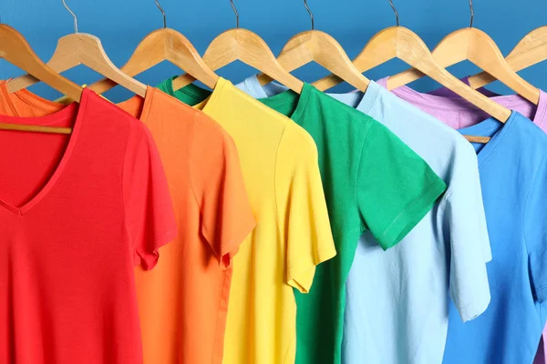 Bright clothes on wooden hangers against blue background. Rainbo