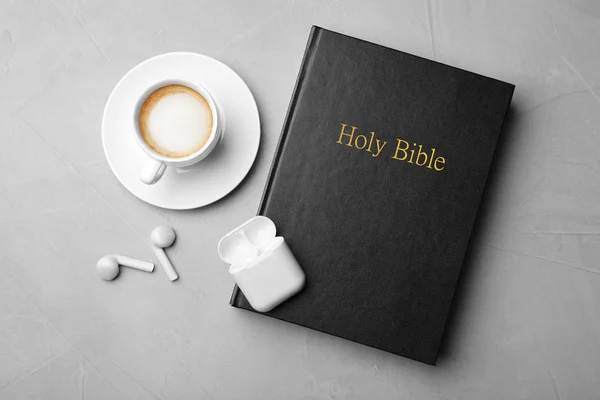 Bible, cup of coffee and earphones on light grey background, flat lay. Religious audiobook