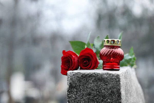 Red roses and candle on grey granite tombstone outdoors. Funeral