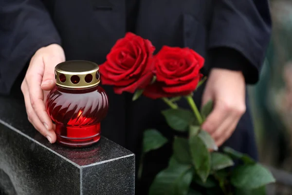 Kvinna som håller röda rosor nära svart granit gravsten med ljus — Stockfoto