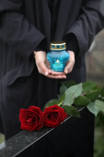 Kvinna med ljus utomhus, fokus på röda rosor. Begravning — Stockfoto