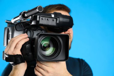 Mavi arkaplanda profesyonel video kamerası olan operatör