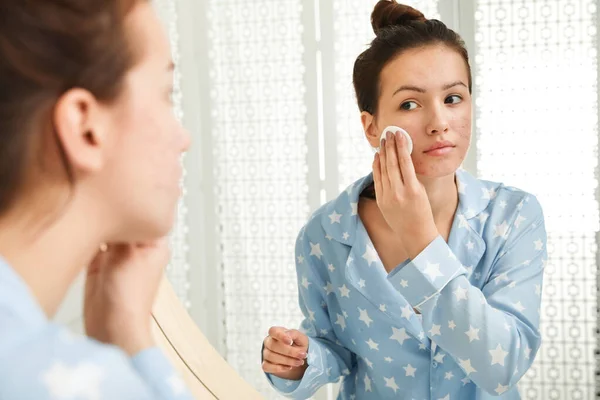 Menina adolescente com problema de acne limpando seu rosto perto do espelho no morcego — Fotografia de Stock