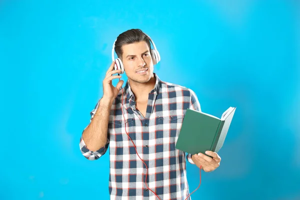 Mann mit Kopfhörer und Buch auf hellblauem Hintergrund. Hörbuch — Stockfoto