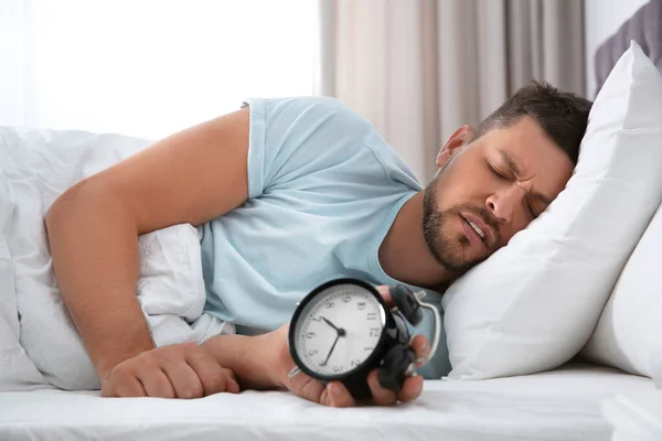 Sleepy man with alarm clock at home in morning — Stock Photo, Image