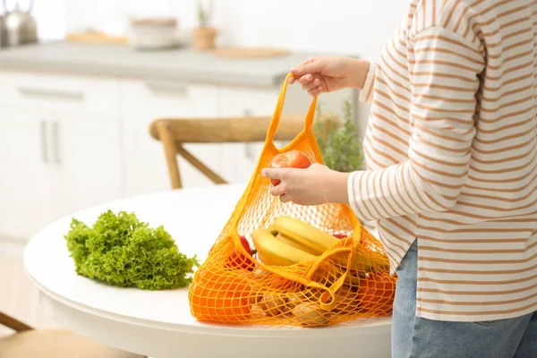 Женщина с чистым мешком фруктов и овощей возле стола на кухне — стоковое фото