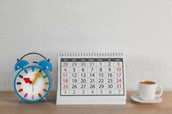 Calendar, alarm clock and cup of coffee on wooden table