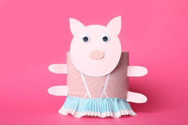 Pembe arka planda tuvalet kağıdı rulosundan yapılmış oyuncak domuz.