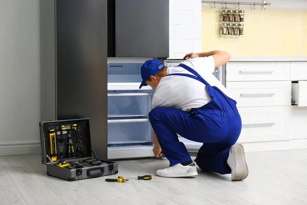 Αρσενικός τεχνικός επισκευάζει χαλασμένο ψυγείο στην κουζίνα — Φωτογραφία Αρχείου