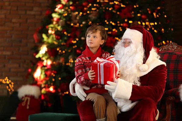 Santa Claus a malý chlapec s dárkem v blízkosti vánočního stromečku uvnitř — Stock fotografie