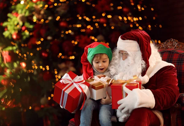 Papá Noel y niño pequeño con regalos cerca del árbol de Navidad interior —  Fotos de Stock