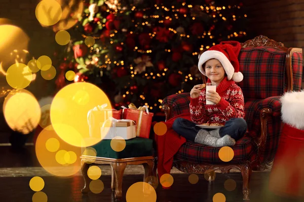 Petit garçon dans le bonnet du Père Noël avec du lait et des biscuits près de Noël — Photo