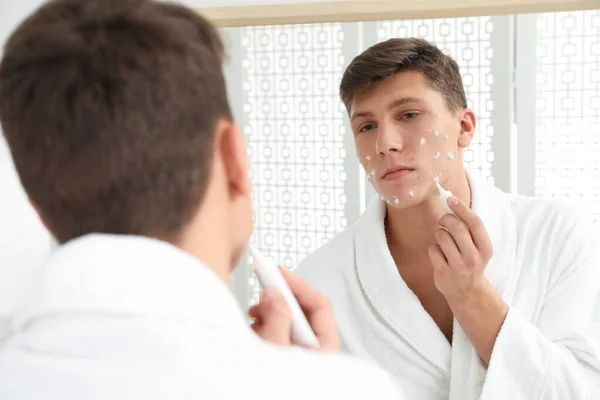 Teen guy with acne problem applying cream near mirror in bathroo — ストック写真
